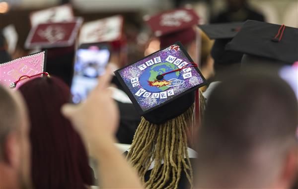 A student wearing a graduation cap with a design of a rocket ship passing by Earth and the text \
